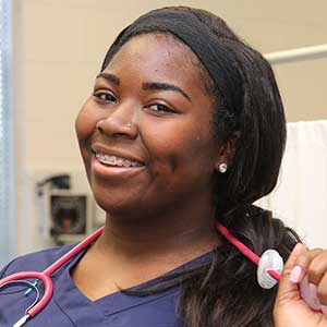 Smiling nurse with stethoscope, wearing blue scrubs in a medical setting.
