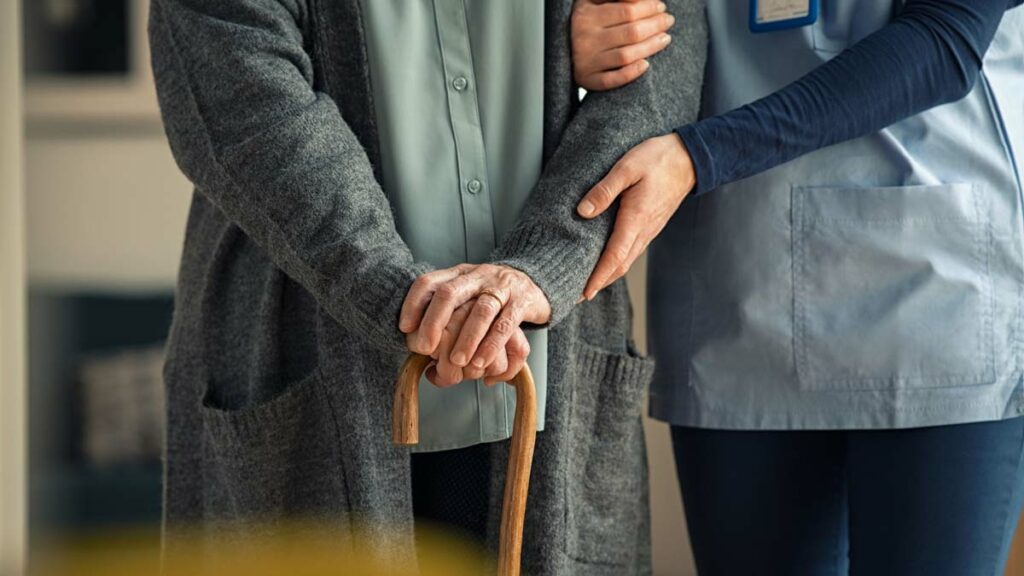 Nursing assistant supporting an elderly person with a cane.