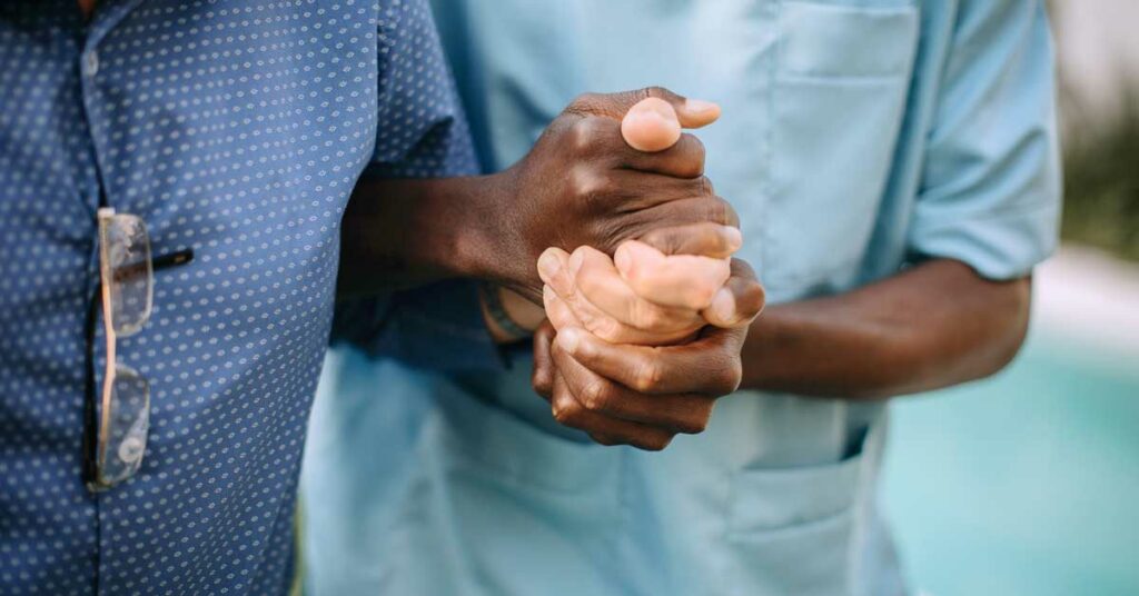 Two people holding hands, one in scrubs, showing care and support.