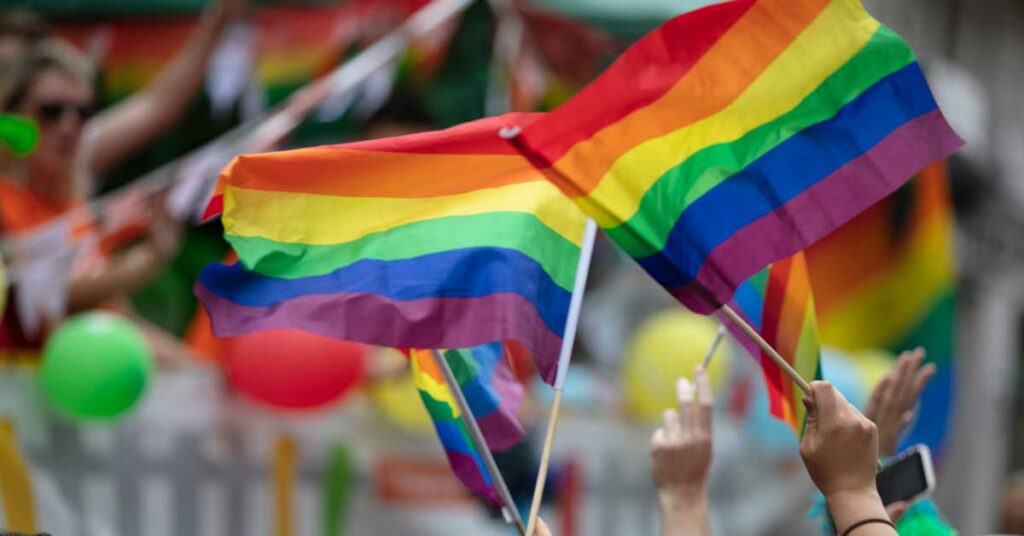 Individuals waving rainbow flags at a lively Pride Month celebration.