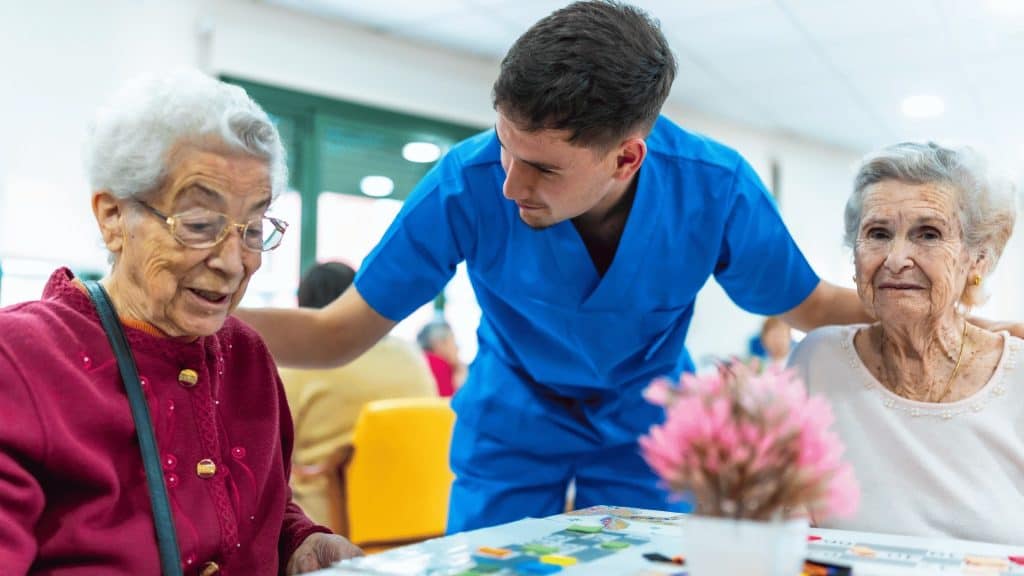 A man in scrubs stands between two older women with his hands on their shoulders